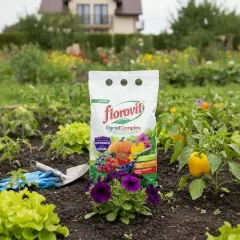 Opakowanie nawozu Florovit OgrodComplex na tle grządki z warzywami i kwiatami.