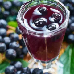 Aronia w kieliszku, jak nalewka z aronii przepis babci. Wokół świeże owoce i liście.