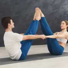 Pareja practicando yoga juntos, realizando posturas para hacer con tu pareja. Se miran sonriendo mientras unen sus pies.