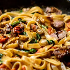 Pâtes tagliatelles avec morceaux de bœuf, tomates cerises, champignons et épinards dans une sauce crémeuse.
