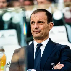 Massimiliano Allegri, w eleganckim garniturze, z rękami skrzyżowanymi na piersi, obserwuje grę.