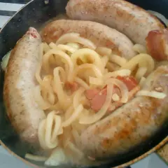 Biała kiełbasa w piwie dusi się z cebulą i boczkiem na patelni.