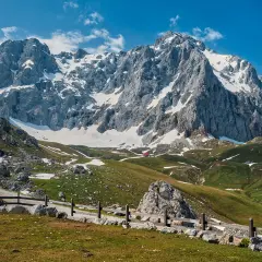 Majestuosas montañas nevadas y verdes praderas invitan al senderismo en los Picos de Europa. Un refugio rojo se asoma entre las colinas.