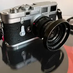 A classic Leica M3 camera with a Leitz Wetzlar lens sits on a reflective surface, ready to capture timeless moments.