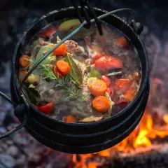 Kociołek z mięsem i warzywami gotujący się nad ogniskiem.