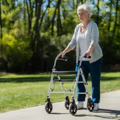 Ältere Frau geht mit Rollator auf Rezept im Park.