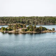 Malutka wyspa z domkiem i drzewami, część archipelagu sztokholmskiego, otoczona spokojną wodą.