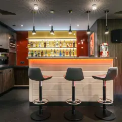 Stilvolle Bar mit beleuchteten Regalen voller Flaschen, drei Barhockern und einer Popcornmaschine. Tolle partyraum bar ideen für Ihr Zuhause.