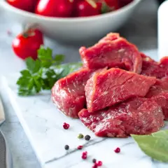 Morceaux de viande rouge crue sur une planche en marbre, avec des tomates cerises et des herbes. Question : viande hors frigo combien de temps ?