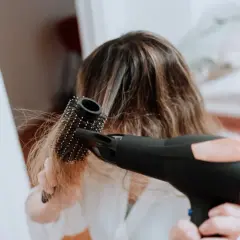 Frau föhnt ihre Haare mit einer Rundbürste, um fliegende Haare zu bändigen.