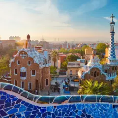 Kolorowa mozaika Parku Güell wita na wspaniałej **barcelona wycieczka**. Dwa bajkowe domki i wieża z krzyżem w tle.