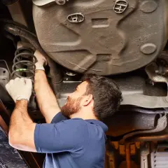 Mecánico revisa el amortiguador de un coche, buscando la causa de un posible ruido copela.