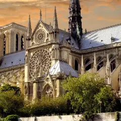Katedra Notre Dame w Paryżu z różanymi oknami i wieżami na tle pomarańczowego nieba.