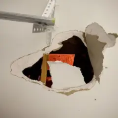 Un **buco nel muro troppo grande** rivela una struttura arancione e un montante di legno.