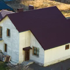 Nowy dom w zabudowie zagrodowej z ciemnobrązowym dachem, otynkowany na biało, z widocznymi materiałami budowlanymi obok.