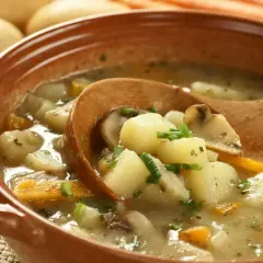 Zupa ziemniaczana przepis babci. Aromatyczna, sycąca zupa z ziemniaków, marchewki i grzybów, podana w glinianej misce z drewnianą łyżką.