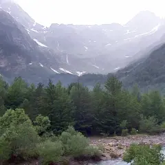 Majestuoso valle Pineta con cascadas cayendo por montañas cubiertas de nieve y un río serpenteando entre frondosos bosques verdes.