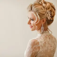 Elegancka panna młoda z upiętymi włosami ozdobionymi perłami i kryształami. Jej fryzury ślubne glamour podkreślają delikatne loki opadające na ramiona.