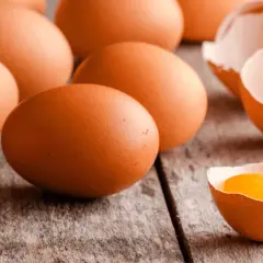 Kilka brązowych jajek, jedno rozbite z widocznym żółtkiem, na drewnianym tle.