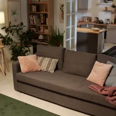 Przytulny salon z szarą kanapą, poduszkami i pledem. Lampy zapewniają ciepłe doświetlenie pomieszczeń, tworząc przytulną atmosferę.