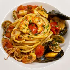Un invitante piatto di spaghetti allo scoglio, con gamberi, cozze, vongole e calamari, condito con pomodorini e prezzemolo.
