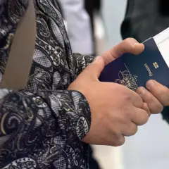 Ręce trzymają paszport i bilet lotniczy. Widoczne są dane do biletu lotniczego, takie jak numer lotu i bramka.