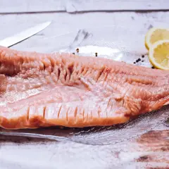 Surowy filet karpia na talerzu z cytryną i pieprzem, obok nóż.