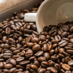 Chicchi di caffè tostati, con una tazzina bianca rovesciata in mezzo. Un'immagine che evoca il piacere del caffè senza caffeina.