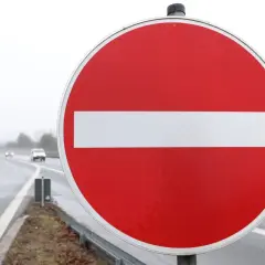 Ein rotes Rundschild mit weißem Balken: durchfahrt verboten schild. Autos fahren auf nasser Straße im Hintergrund.