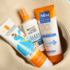 Trois tubes de crème solaire, dont une crème solaire périmée, sont posés sur un chapeau de paille.