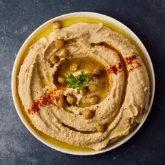 Cremoso hummus di ceci guarnito con ceci interi, paprika e prezzemolo, pronto per essere gustato.