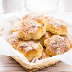 Koszyk pełen puszystych ciastek z serem twarogowym, posypanych cukrem. Idealne na śniadanie lub podwieczorek.