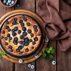 Bizcocho de arándanos casero, recién horneado y adornado con arándanos frescos y hojas de menta sobre una mesa de madera rústica.