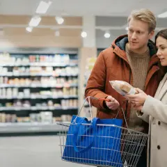Para ogląda produkty w sklepie spożywczym, trzymając koszyk.