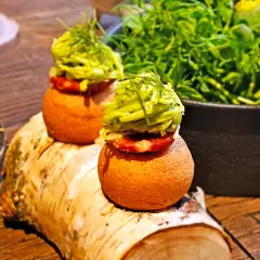Dwa apetyczne mini-burgerki z zielonymi dodatkami, serwowane na pniu brzozy. Idealne na przekąskę, jak w najlepszych **bottiglieria 1881 opinie**.