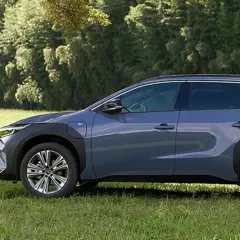 Szary Subaru Solterra stoi na trawie obok drewnianej huśtawki i drzew.