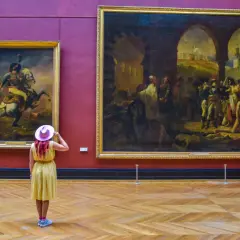 Kobieta w żółtej sukience i różowym kapeluszu podziwia obrazy w Luwrze. Co to za muzeum? To słynny paryski Luwr!
