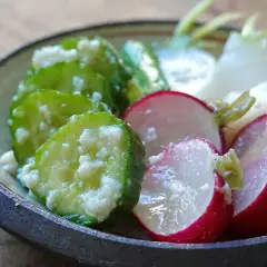 A close-up of a bowl filled with shio koji pickles. Sliced cucumbers and radishes are coated in a creamy marinade, showcasing their vibrant colors and textures.