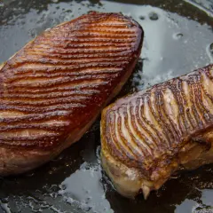 Deux magrets de canard grillés dans une poêle, prêts pour une recette savoureuse. La peau est dorée et croustillante.
