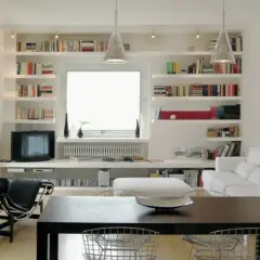 Librerie in cartongesso moderne con libri, TV, divano bianco e tavolo da pranzo.