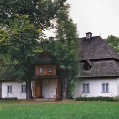 Dwór w Łopusznej otoczony zielenią, z charakterystycznym drewnianym gankiem i dwuspadowym dachem krytym gontem.
