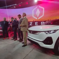 Prezentacja nowoczesnego izera samochód. Na scenie stoi biały i czerwony model, obok nich grupa mężczyzn w garniturach.