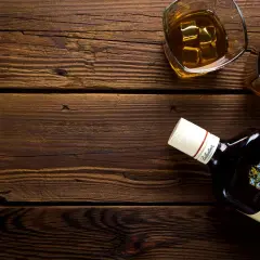 Butelka Ballantine's i dwa kieliszki z whisky na drewnianym stole. Pamiętaj o chorwacja limity alkoholu podczas podróży.