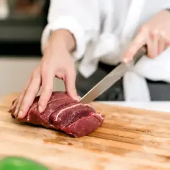 Kobieta kroi surowe mięso na desce. To część przygotowań do diety lwa, która stawia na białko.