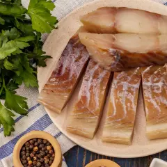 Kawałki wędzonego dorsza czarnego na talerzu, obok pęczek natki pietruszki i miseczka z pieprzem.