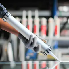 Demostración de como usar una pistola de silicona para aplicar un cordón uniforme sobre una superficie de vidrio.