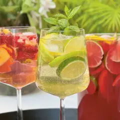Tre glas med alkoholfri sangria fyllda med frukt och is. En kanna med röd sangria i bakgrunden.