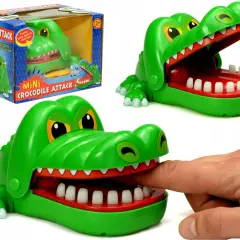 Zielona zabawka gra krokodyl z otwartą paszczą, do której włożono palec. Obok pudełko z napisem "Mini Crocodile Attack".