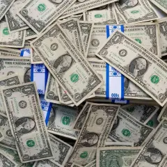 Stosy banknotów jednodolarowych i paczki z napisem "100". To obraz księgowania millenium, gdzie pieniądze odgrywają kluczową rolę.