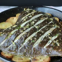 Rodaballo al horno con patatas, preparado con cortes y aderezado con hierbas y ajo.